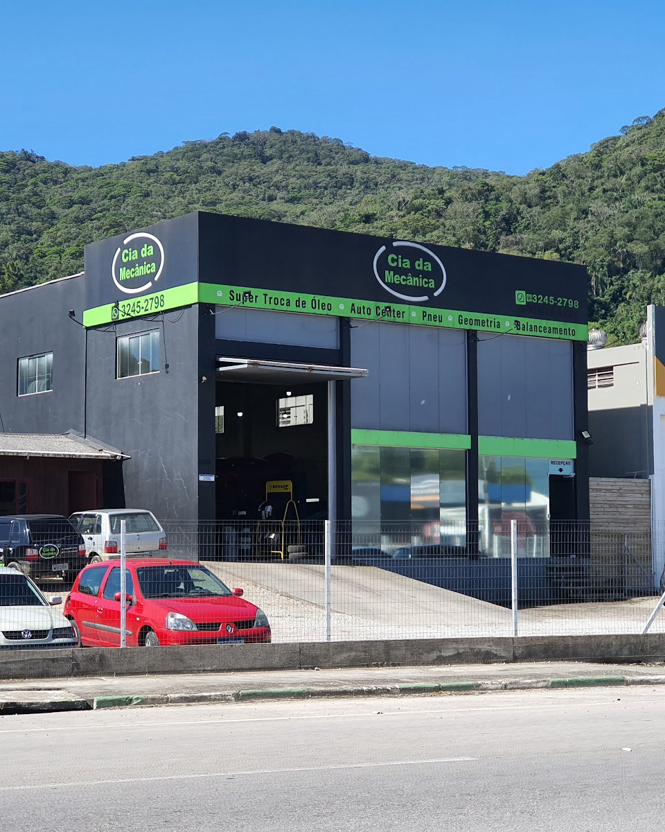 Fachada da Cia da Mecânica, prédio preto com faixa verde, a logo no alto e o morro verde atrás