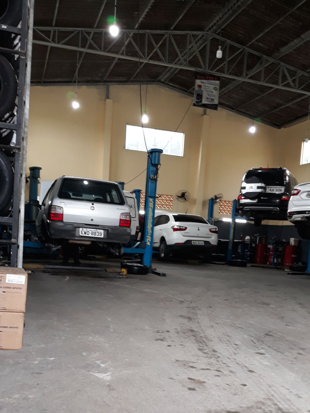 Salão da oficina com elevadores azuis, carros erguidos e pneus na estante à esquerda