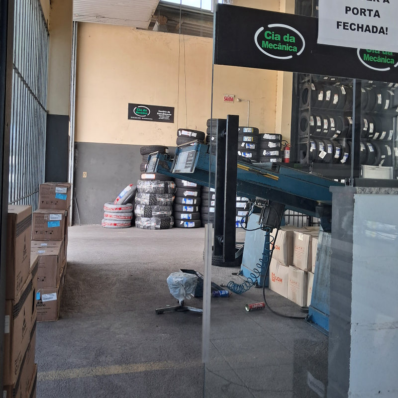 Estante cheia de pneus dentro da oficina, com a placa da Cia da Mecânica na parede